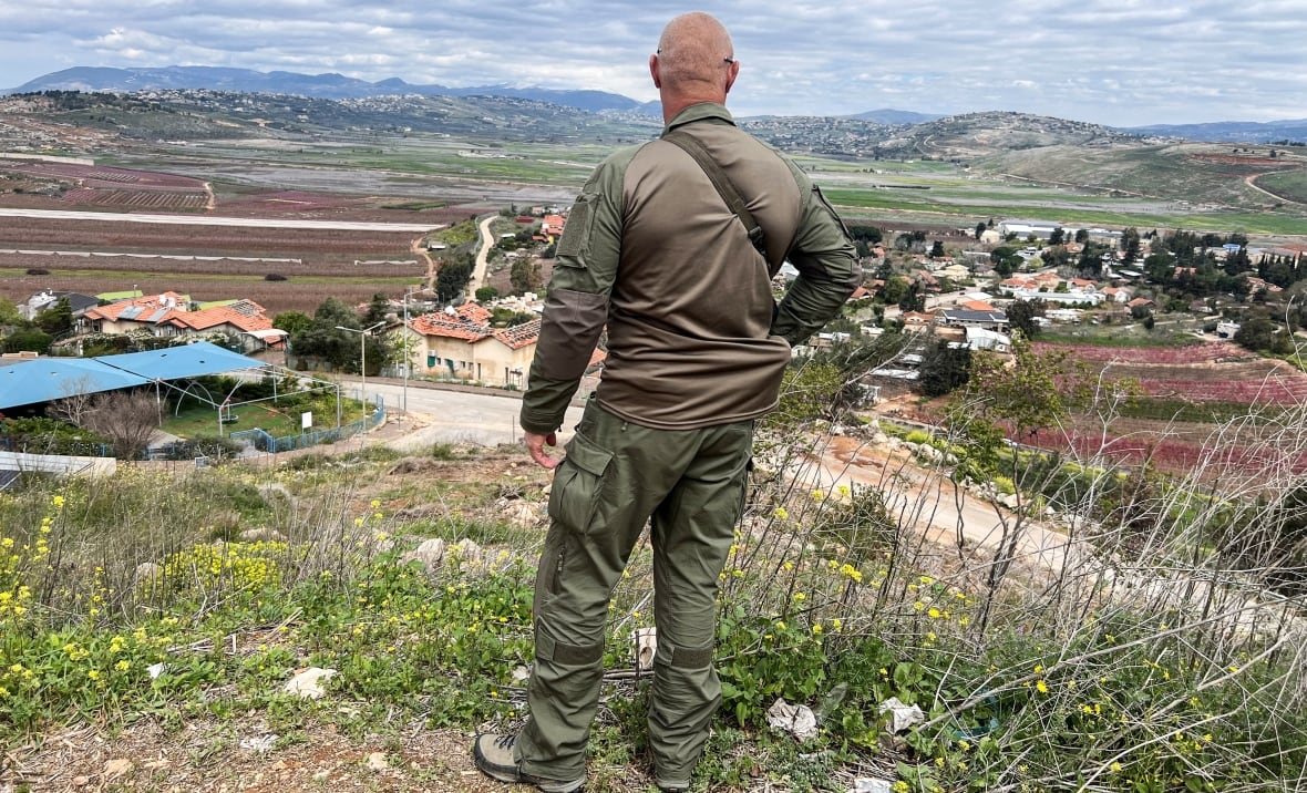 A soldier stands atop a hill overlooking a town.