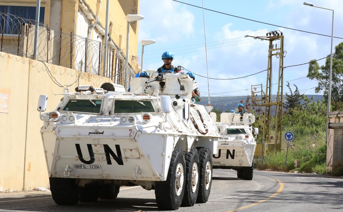 Soldiers in armoured trucks traverse a road next to a border wall.