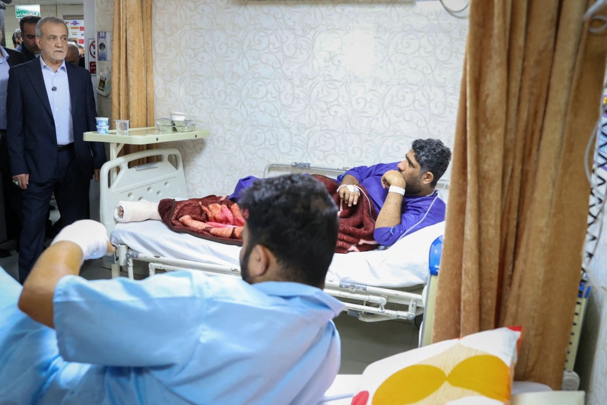 Patients on hospital beds sit up to greet someone entering their room.