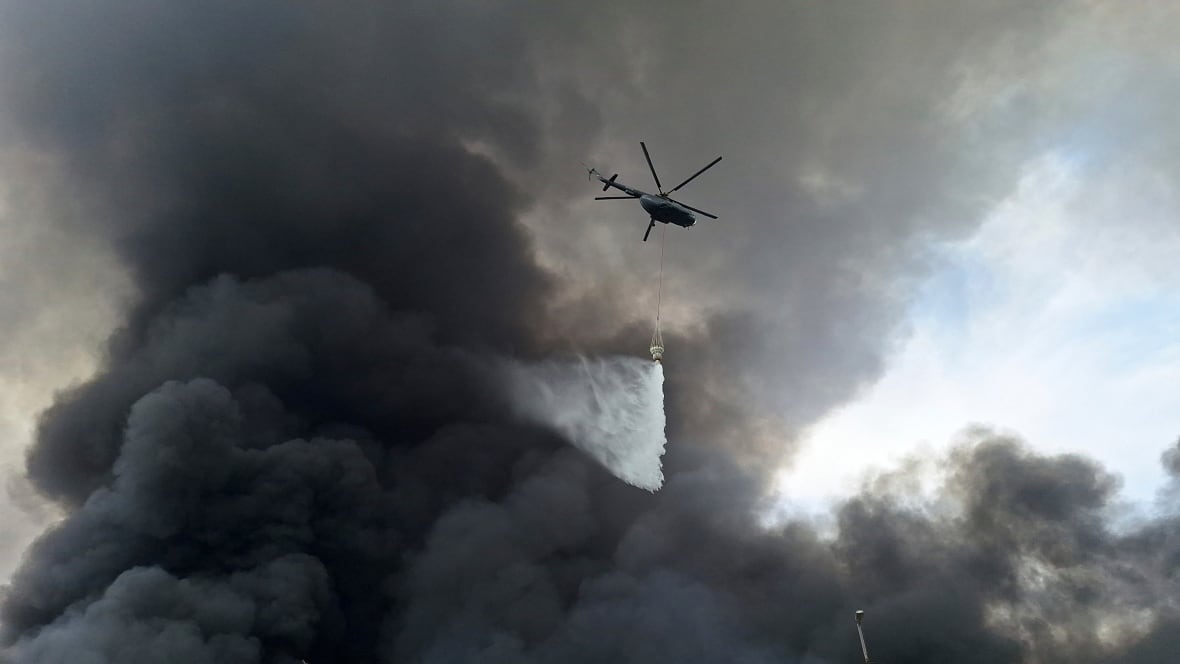 Iran president visits injured, calls for probe into port explosion that killed dozens A helicopter flying amid black smoke drops water.